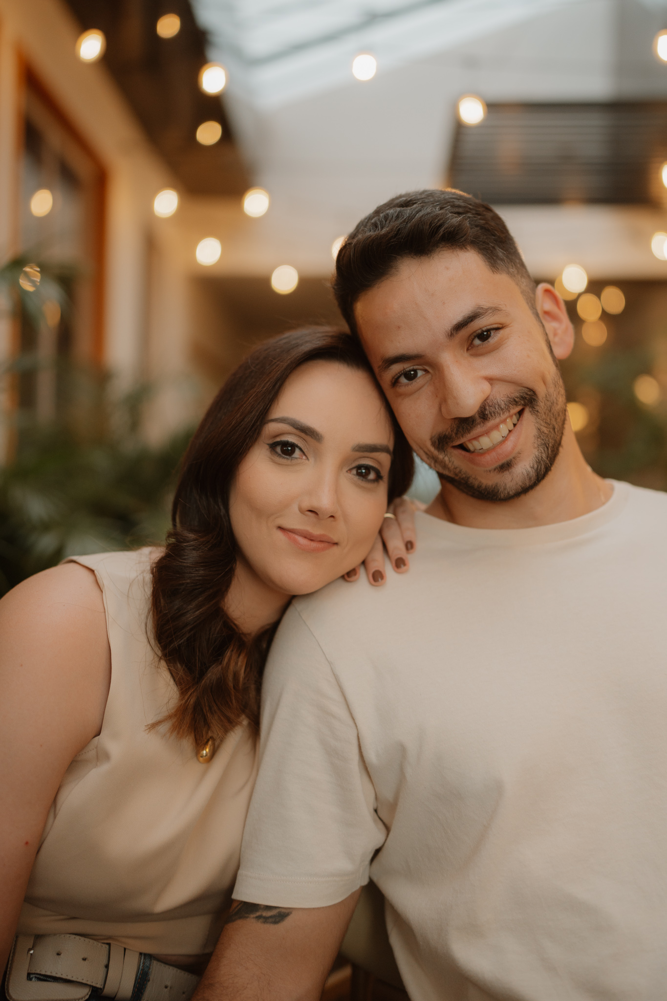 Casal sorrindo e posando abraçado em ambiente de café aconchegante durante ensaio romântico em Presidente Prudente e região
